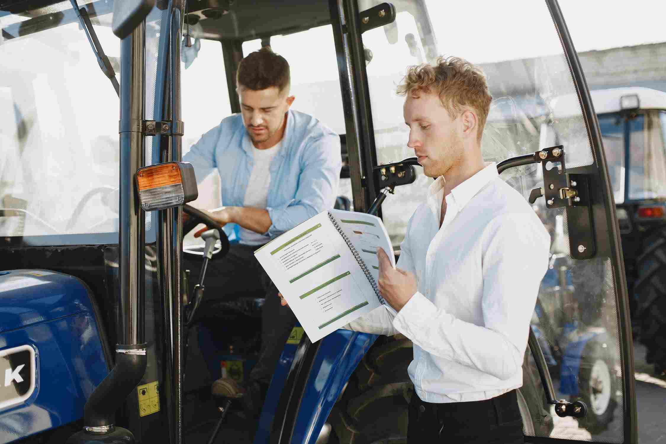 Two co-workers on a construction site, one operating a forklift and the other holding a workbook.